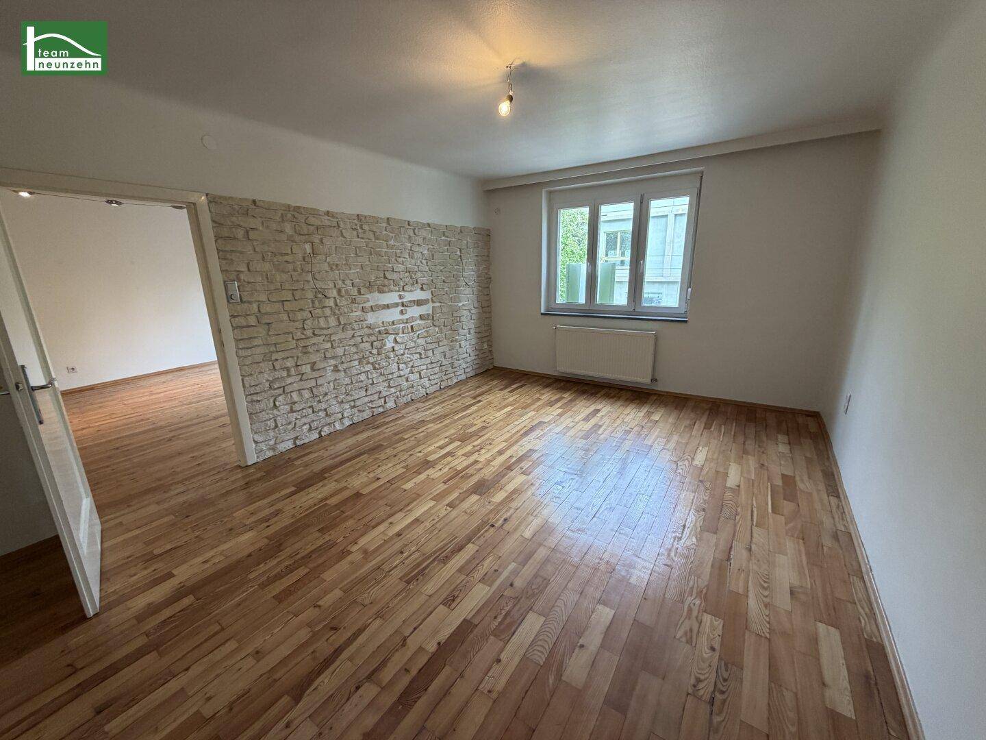 Geräumiges Zimmer mit Holzparkettboden und einer dekorativen Steinwand als Akzent.