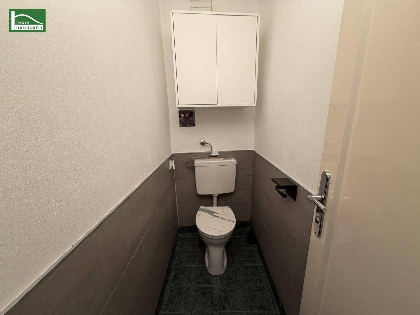 Separate Gästetoilette mit Wand-WC, Fliesenboden und einem kleinen Hängeschrank.