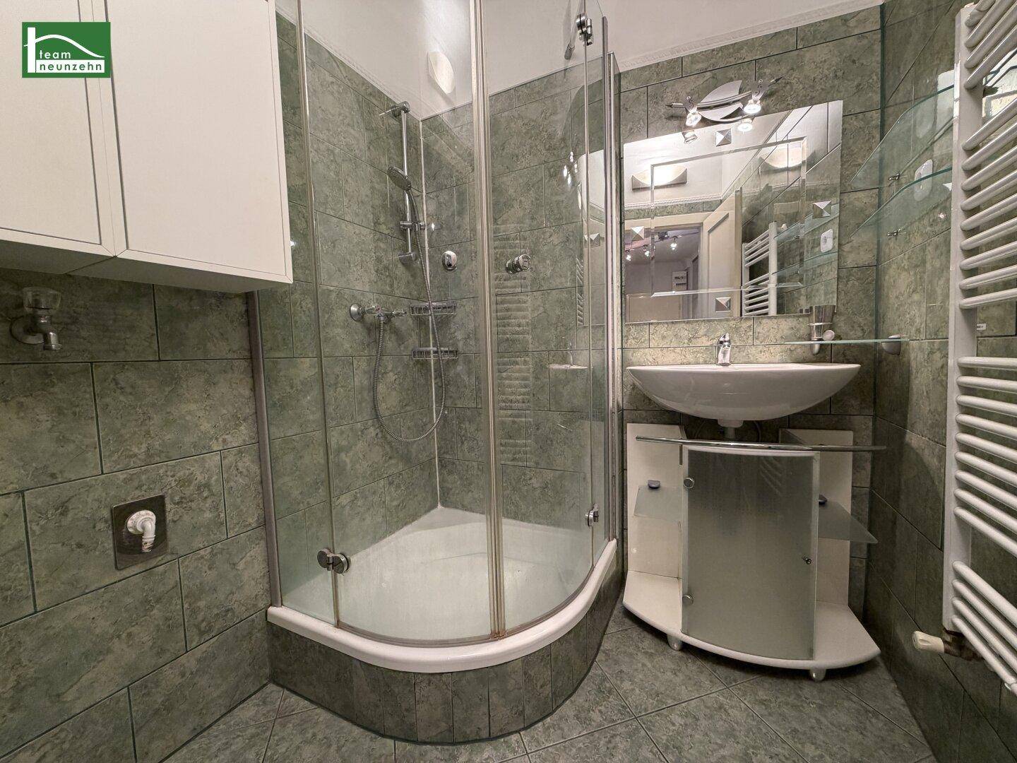 Modernes Badezimmer mit grünen Fliesen, einer Duschkabine und einem Waschbecken mit Spiegel.
