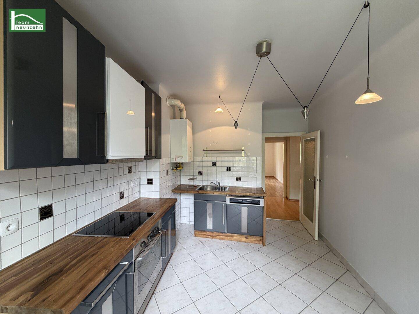 Offene Küche mit modernen grauen Schränken, Holz-Arbeitsplatten und Fliesenboden.