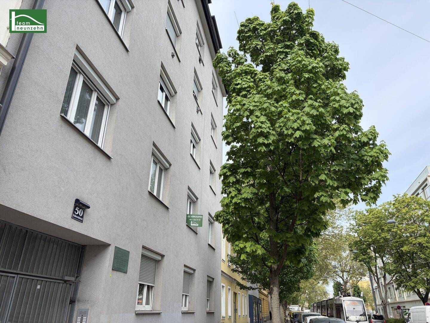 Seitenansicht des Wohngebäudes mit Hausnummer 50 und einem großen, grünen Baum davor.