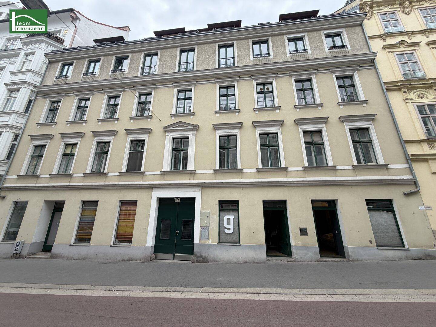 Historische Fassade eines Mehrfamilienhauses mit vielen Fenstern und Geschäften im Erdgeschoss.