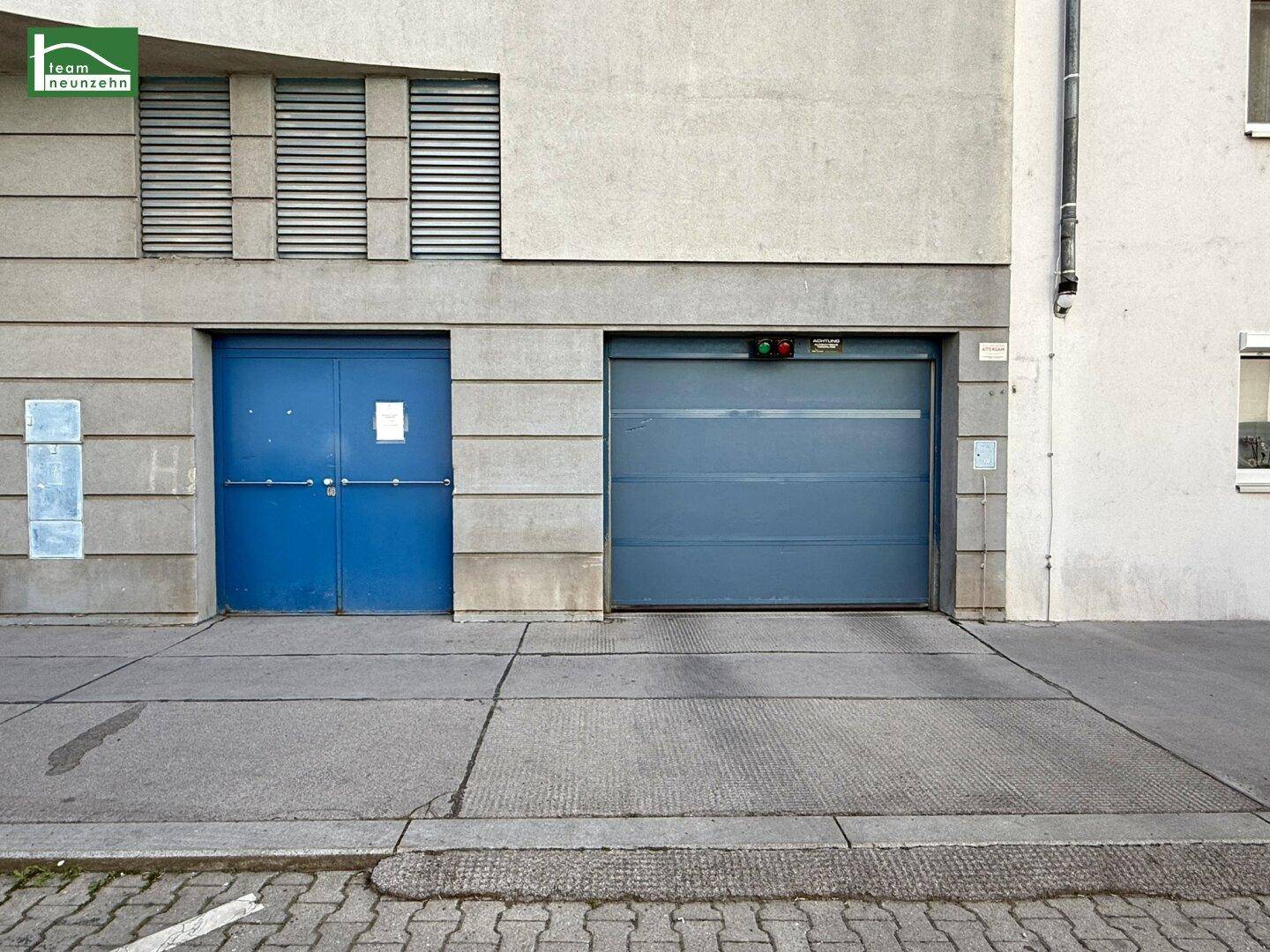 Eingangsbereich des Gebäudes mit blauer Tür und Garagentor auf Straßenniveau.