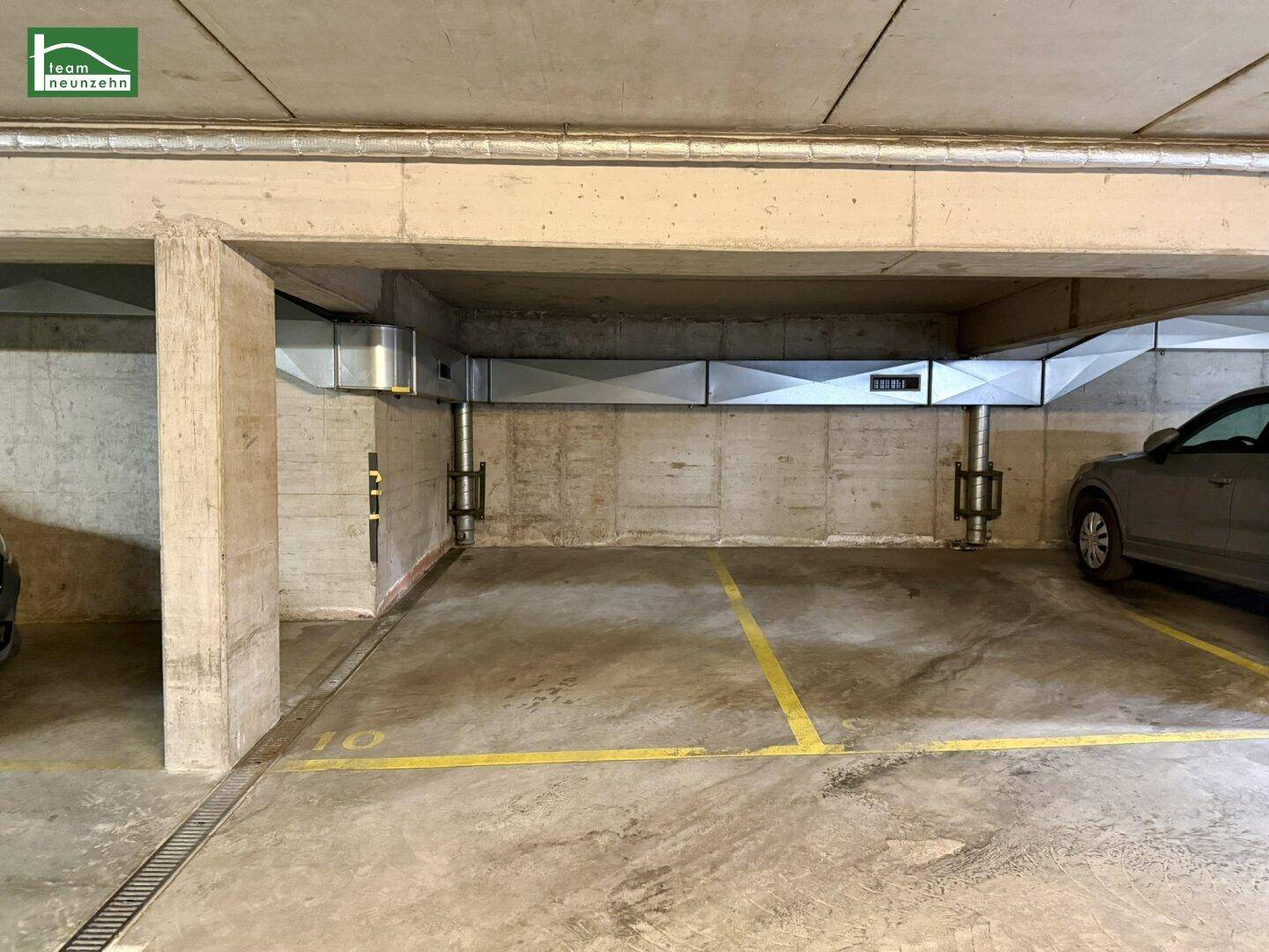 Tiefgaragenstellplatz mit sichtbaren Lüftungsrohren und Betonwänden sowie gelben Markierungen.