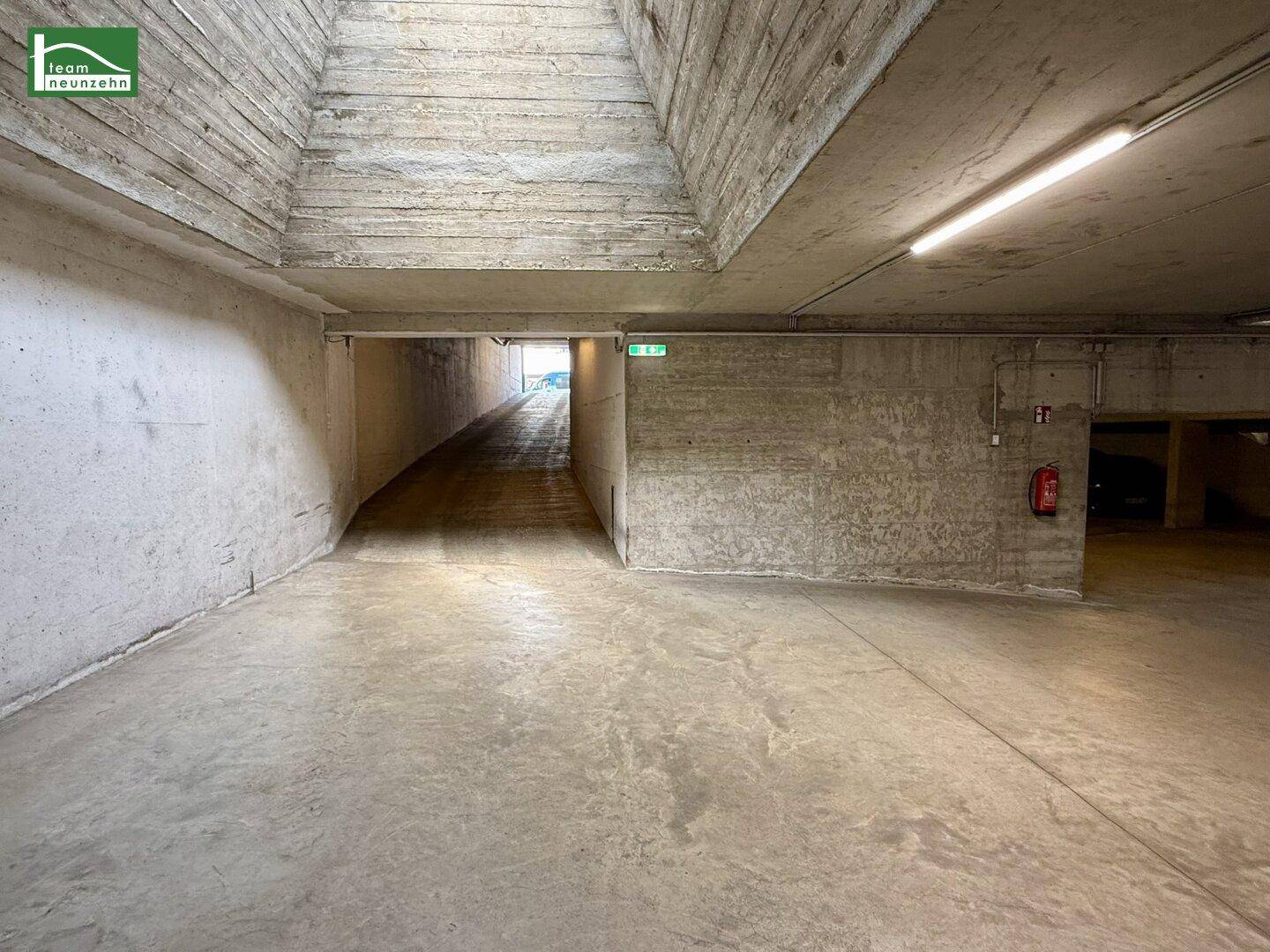 Einfahrtsrampe zur Tiefgarage mit Betonwänden und Beleuchtung, führt in den Untergrund.