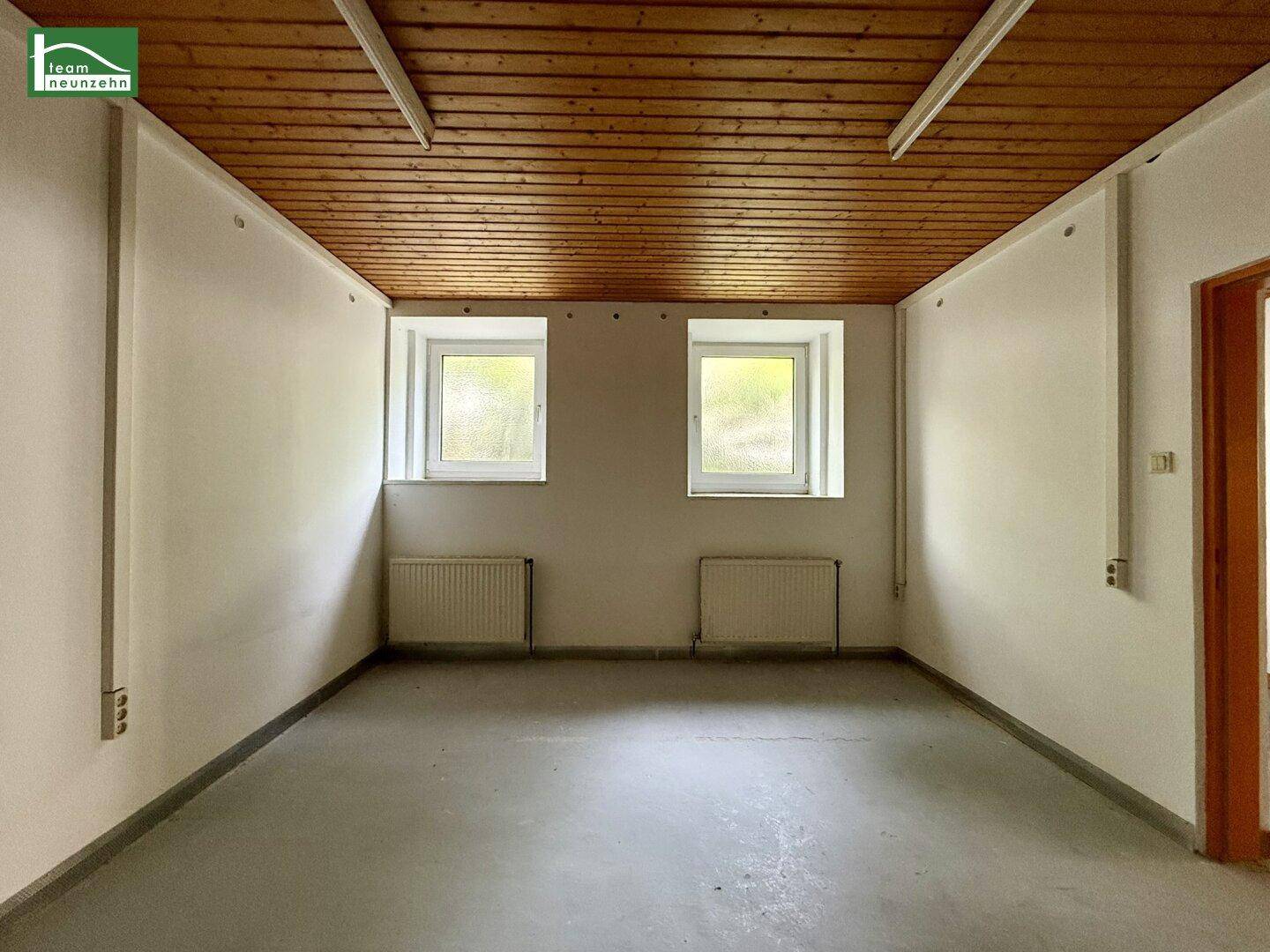 Leerer Raum mit Holzdecke, zwei kleinen Fenstern und einem einfachen Betonboden, ideal für Renovierung.