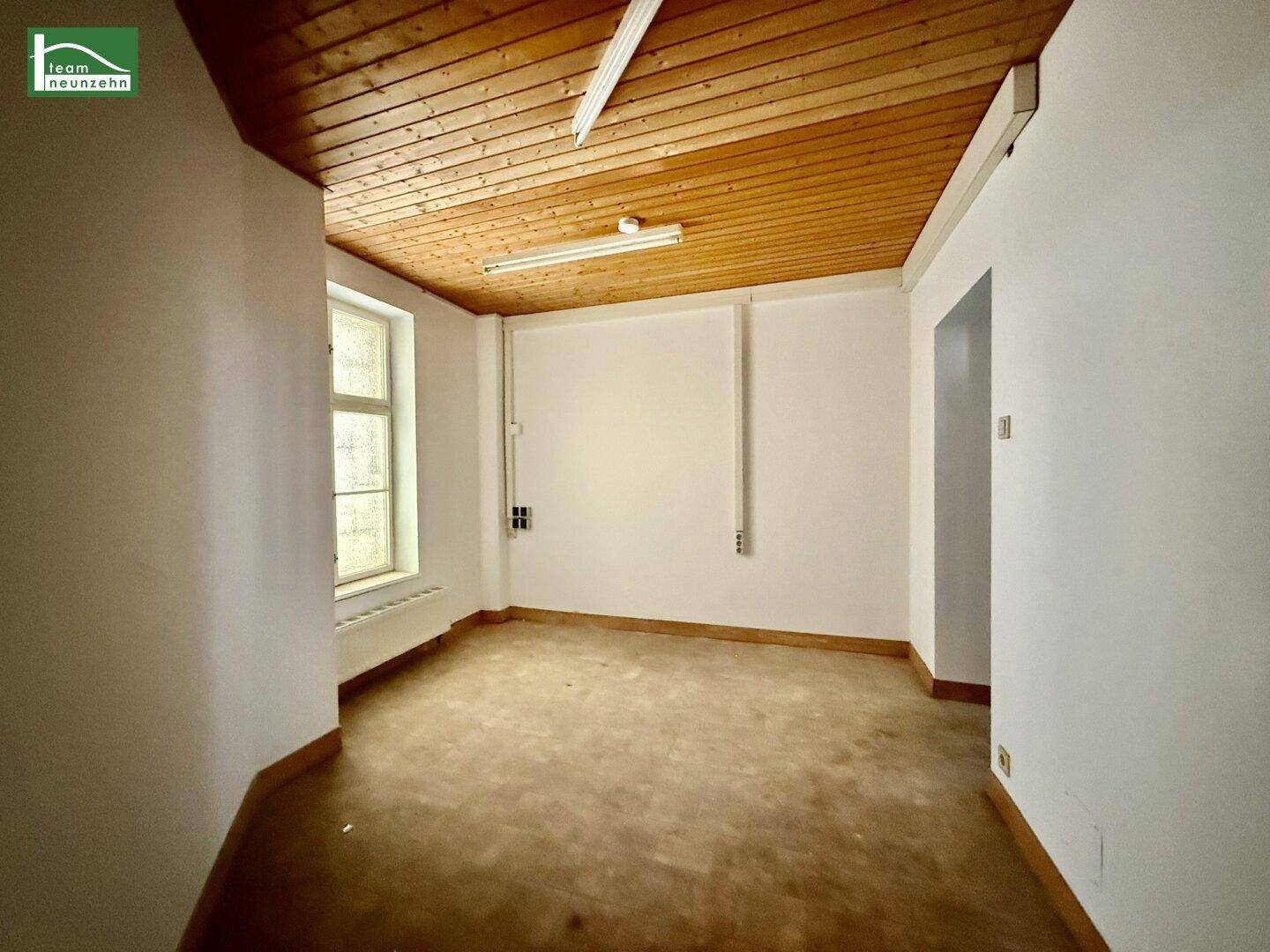 Leerer Raum mit Holzdecke, einem Fenster und einfacher Ausstattung, bereit für individuelle Gestaltung.