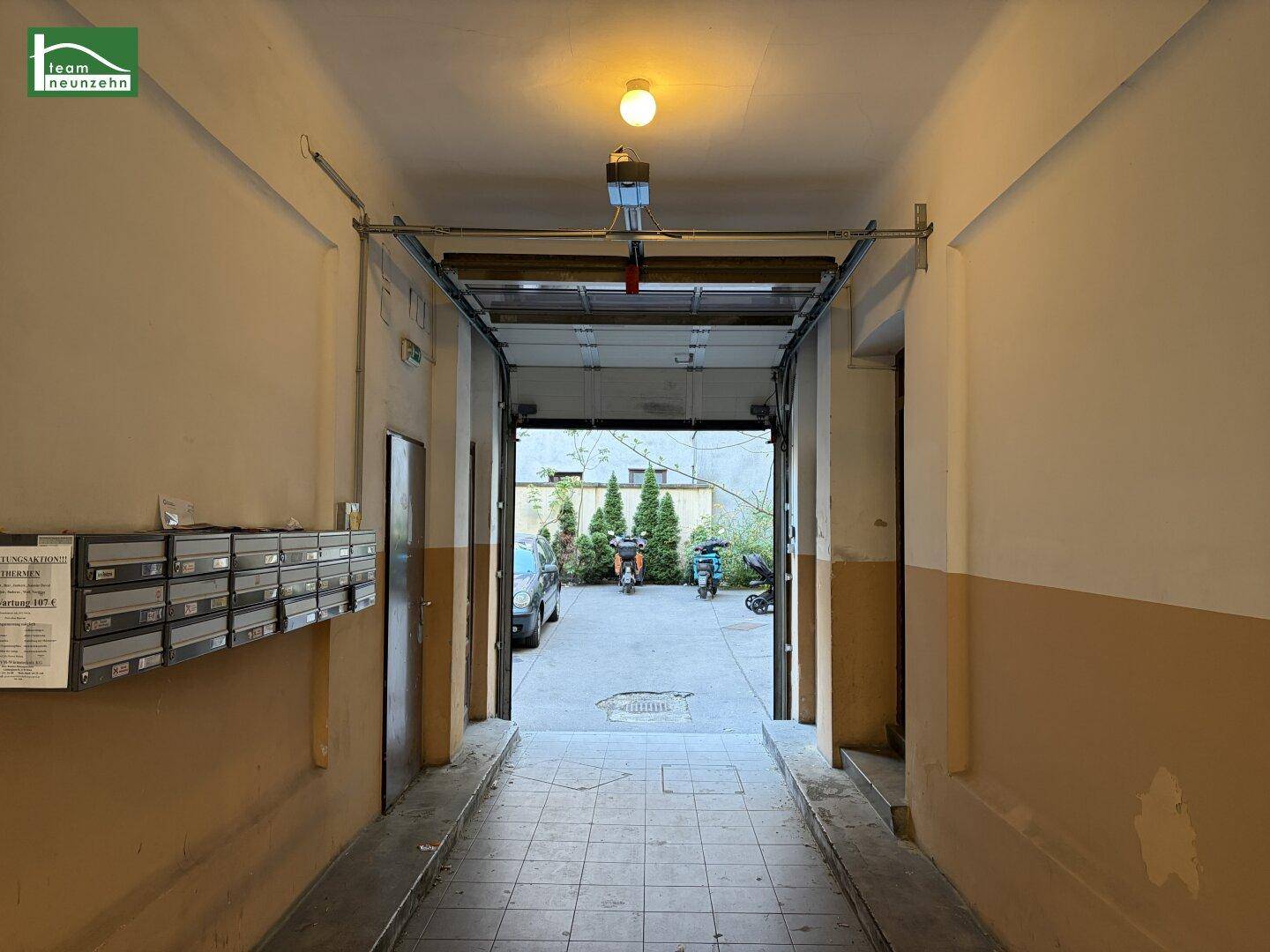 Eingangsbereich mit Briefkästen und Durchgang zum Innenhof, beleuchtet von einer Deckenlampe.