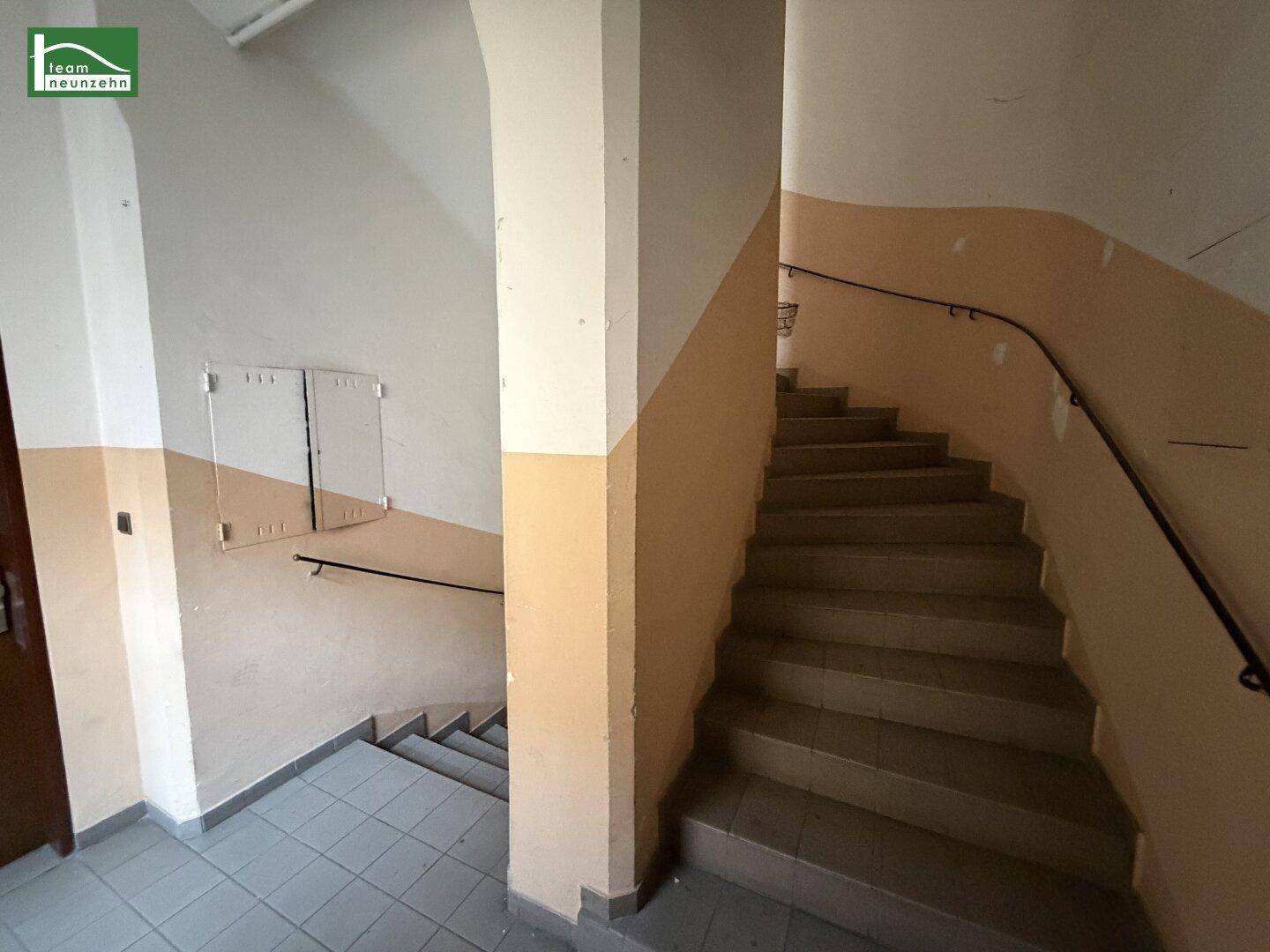 Treppenhaus eines Altbaus mit beigefarbenen Wänden und einem Handlauf.