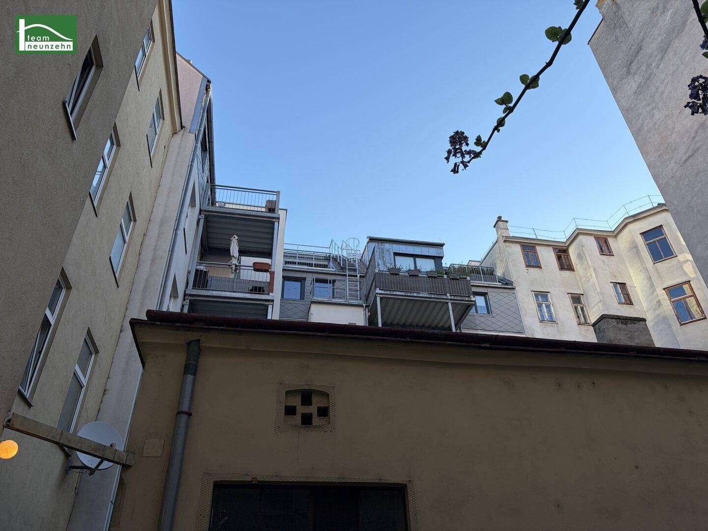 Blick nach oben im Innenhof, zeigt die oberen Stockwerke mit Balkonen und Dachterrassen.