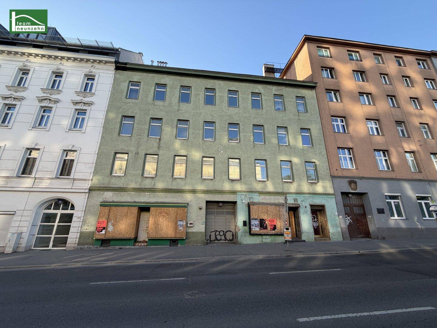 Vorderansicht eines Mehrfamilienhauses mit Geschäften im Erdgeschoss und Wohnungen darüber.