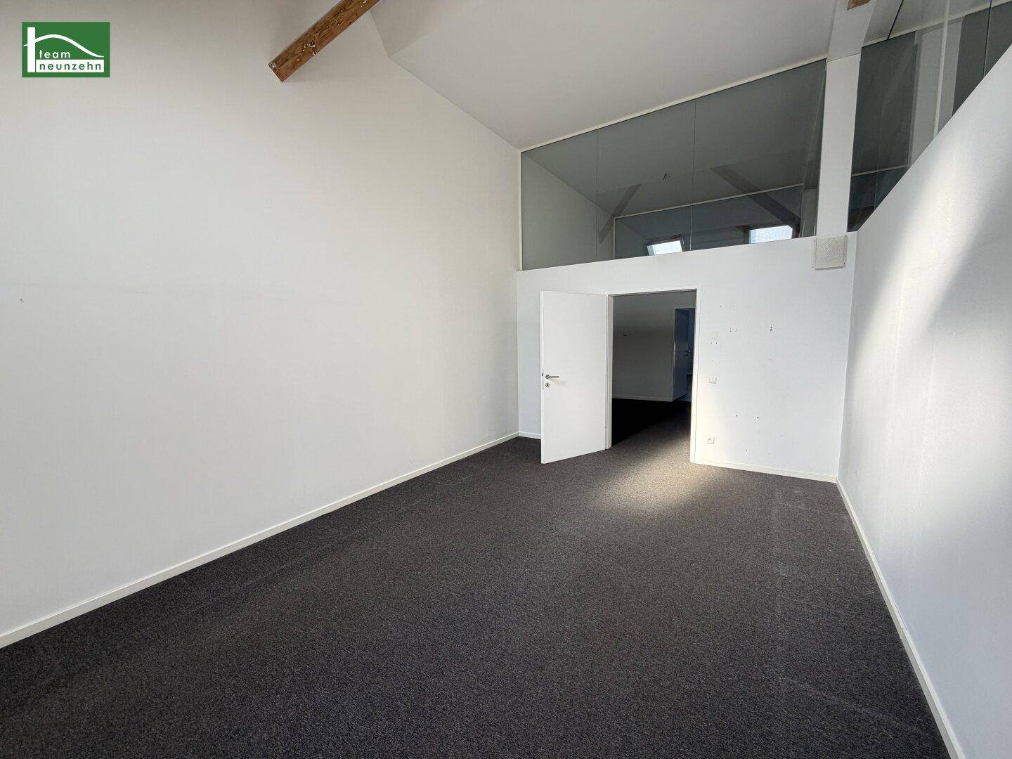 Geräumiger, heller Raum mit Teppichboden, hohen Decken und sichtbaren Holzbalken, ideal für vielseitige Nutzung.