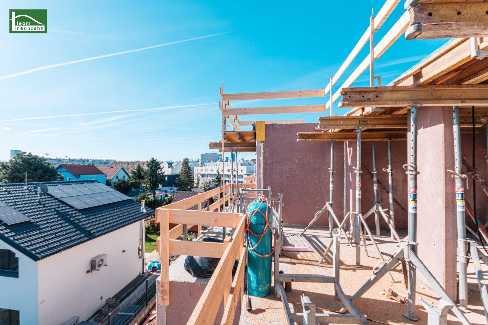 Blick von einem im Bau befindlichen Balkon auf die umliegende Wohngegend mit Solaranlagen auf Dächern.