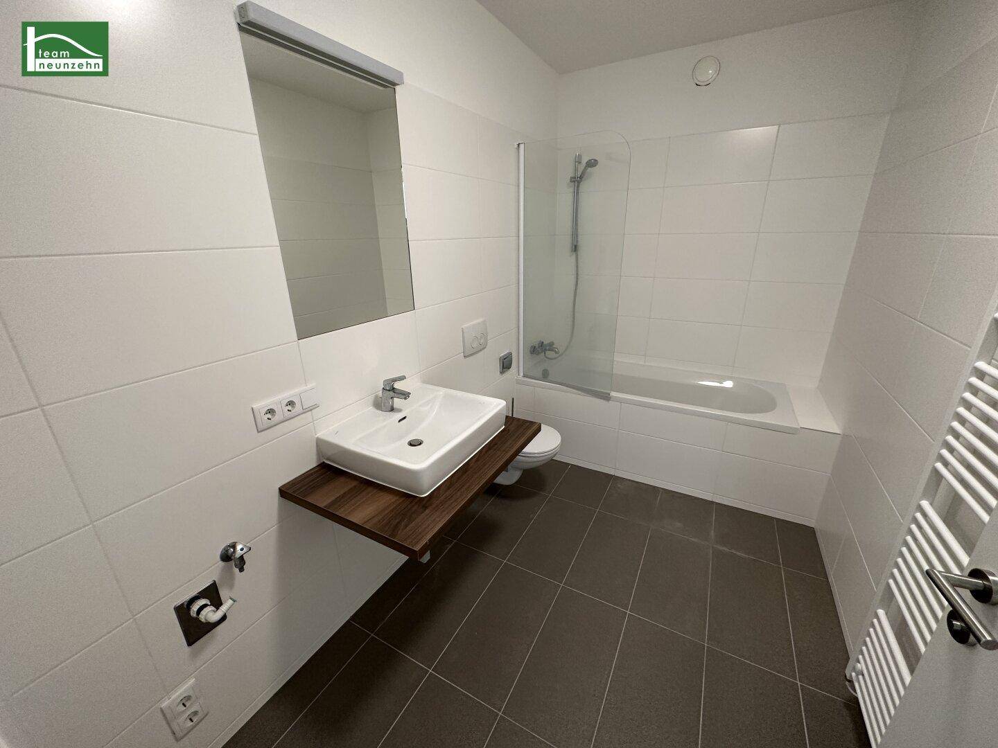 Modernes Badezimmer mit Badewanne, Dusche und Einzelwaschbecken auf dunklem Fliesenboden.