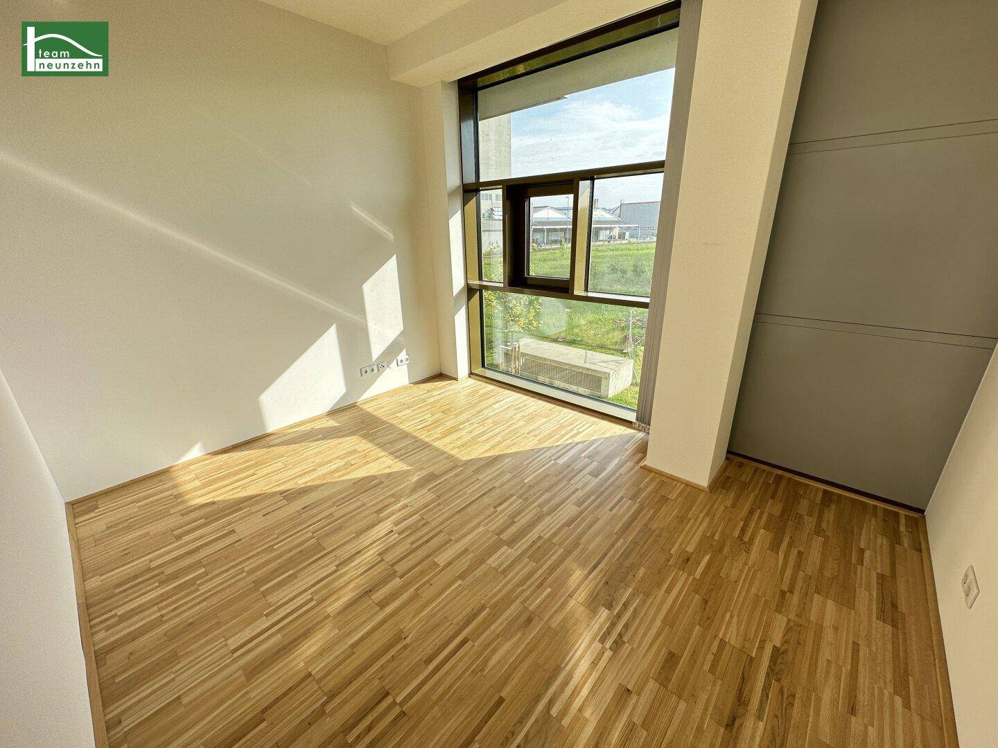 Lichtdurchfluteter Raum mit bodentiefen Fenstern und Holzboden, ideal für Wohnzwecke.