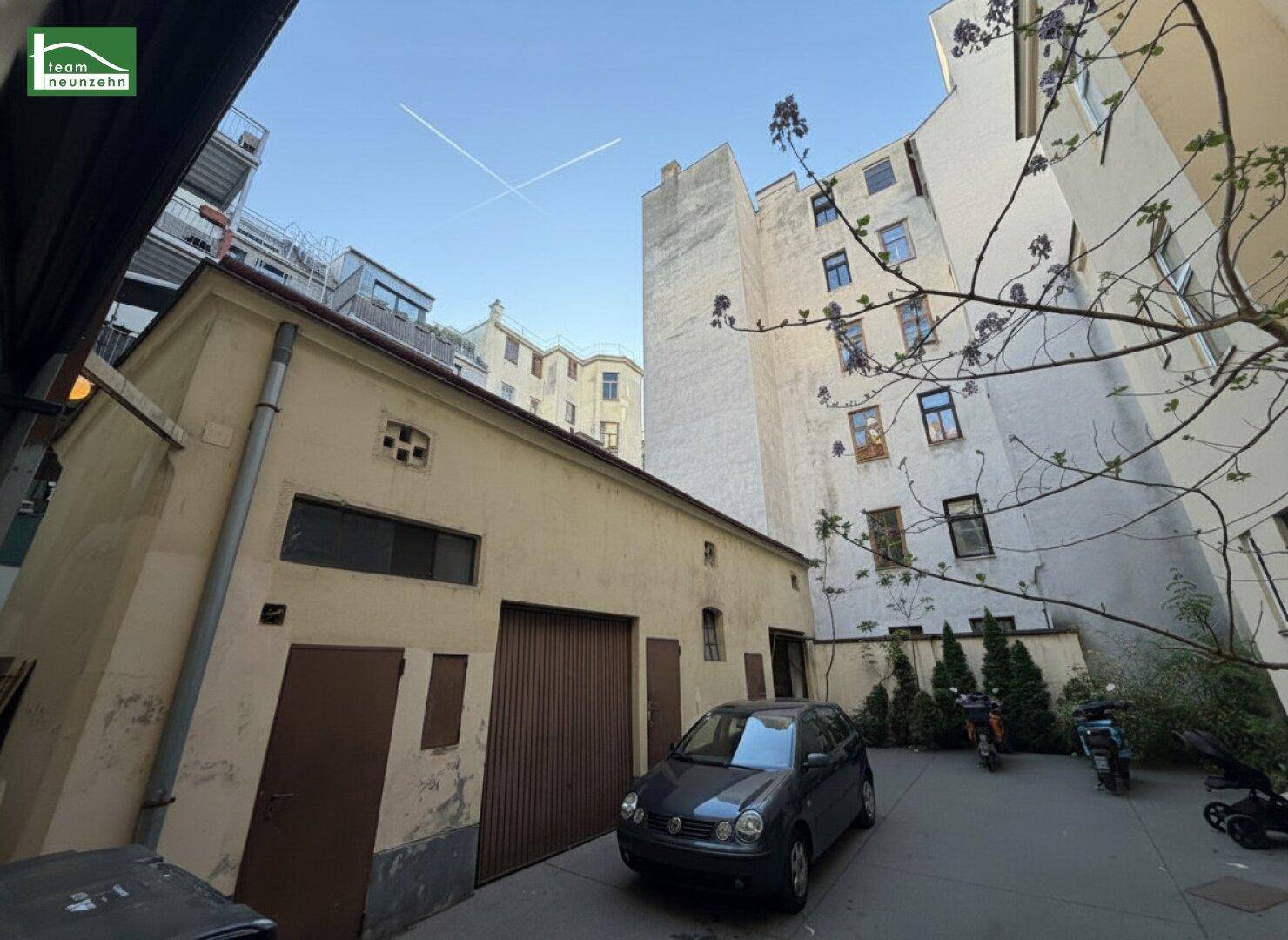 Blick in den Innenhof mit einem kleinen Gebäude, parkenden Fahrzeugen und umliegenden Fassaden.