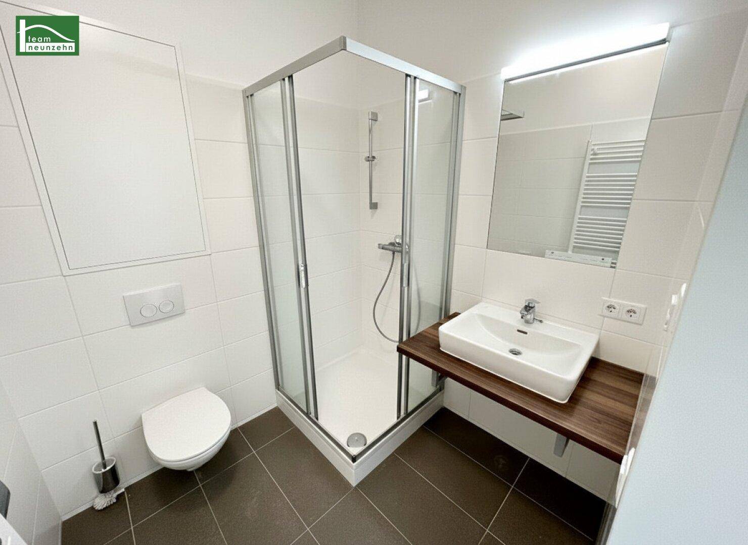 Modernes Badezimmer mit Duschkabine, WC und Einzelwaschbecken auf dunklem Fliesenboden.