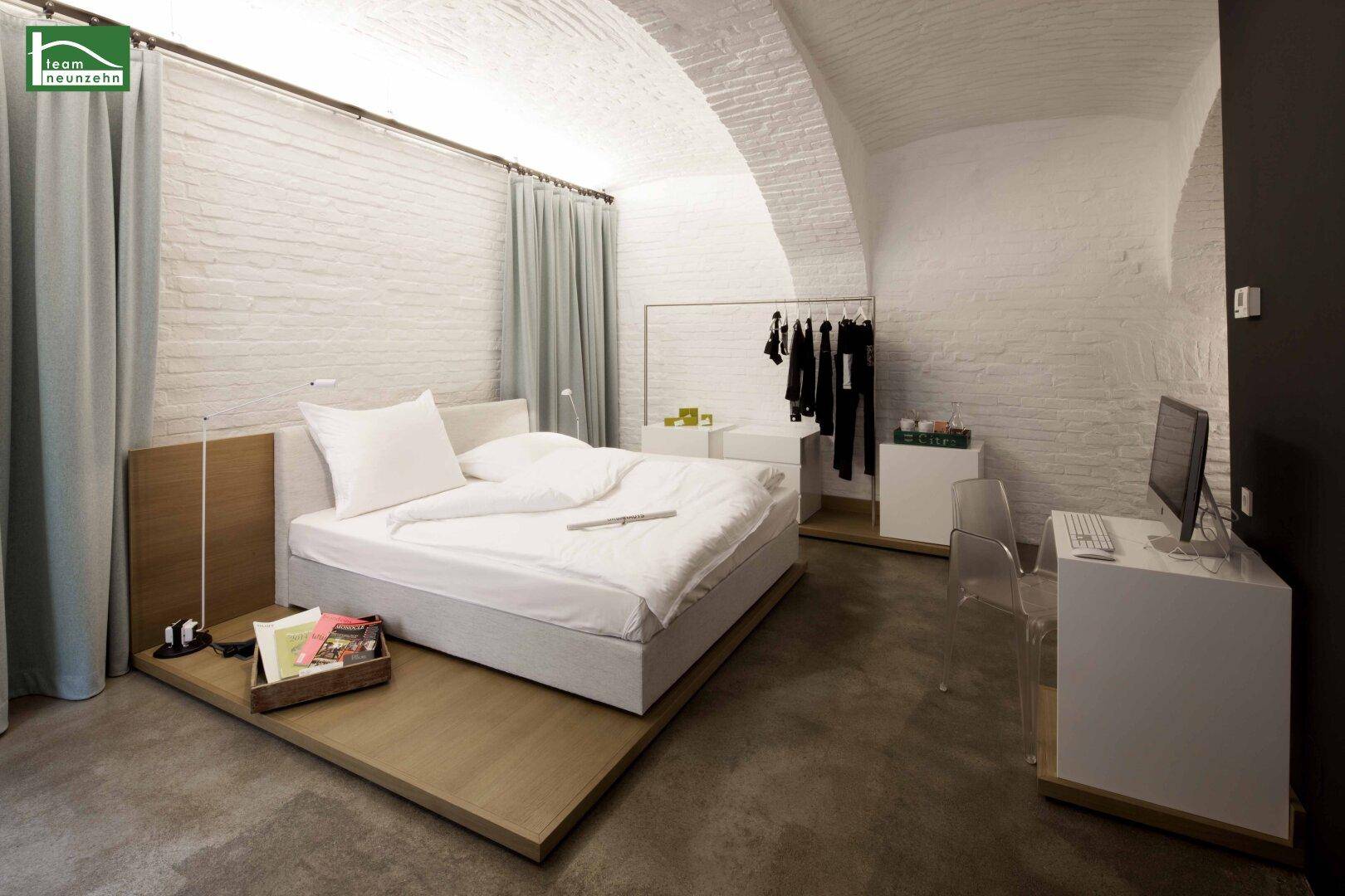 Helles Schlafzimmer mit modernem Bett, Schreibtisch und offenem Kleiderschrankbereich.