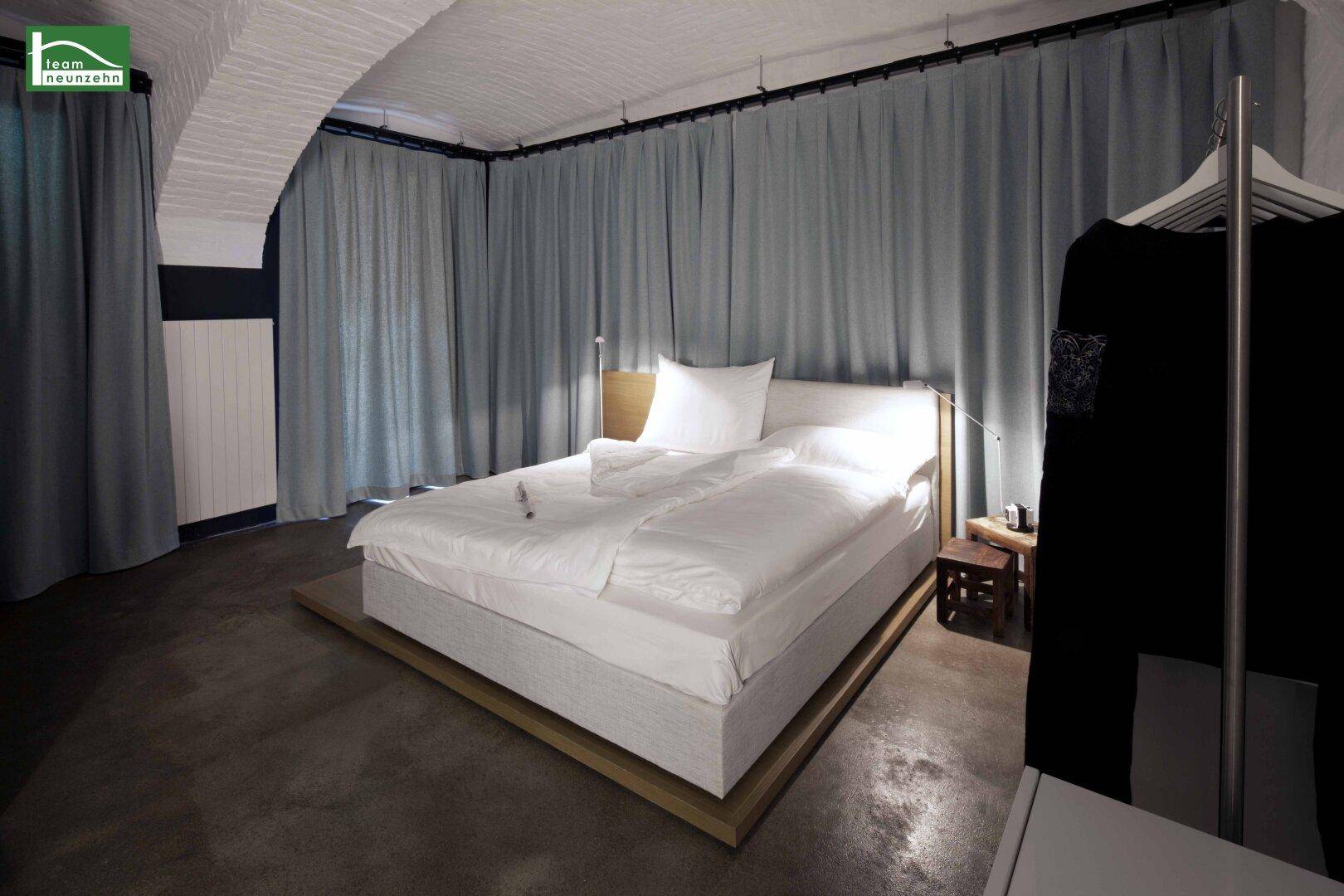 Gemütliches Schlafzimmer mit großem Bett, Vorhängen und indirekter Beleuchtung.