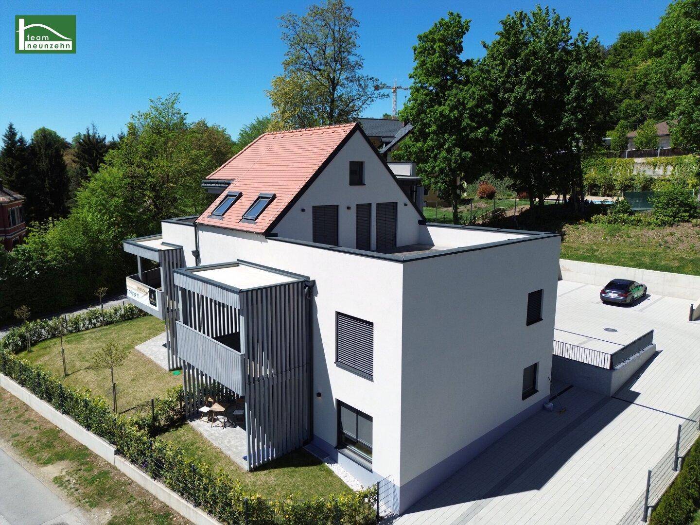 Moderne Wohnanlage mit weißer Fassade, rotem Dach und gepflegtem Gartenbereich.