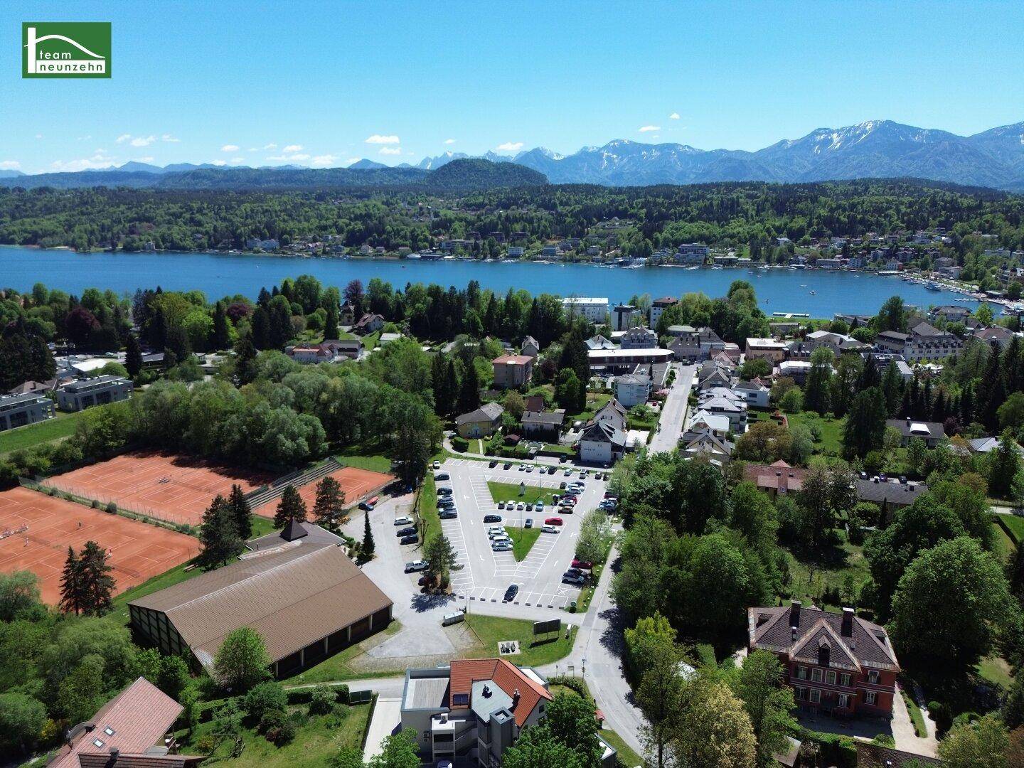 Weitläufige Luftaufnahme der Umgebung mit See, Bergen und Tennisplätzen.