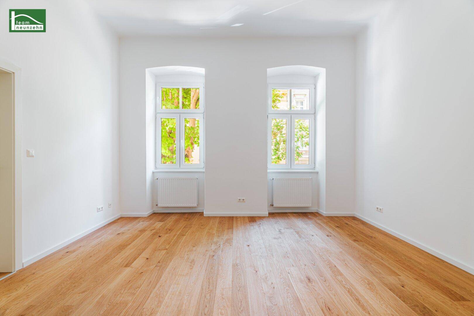 Lichtdurchfluteter Raum mit zwei hohen Fenstern und neuem Holzparkettboden.