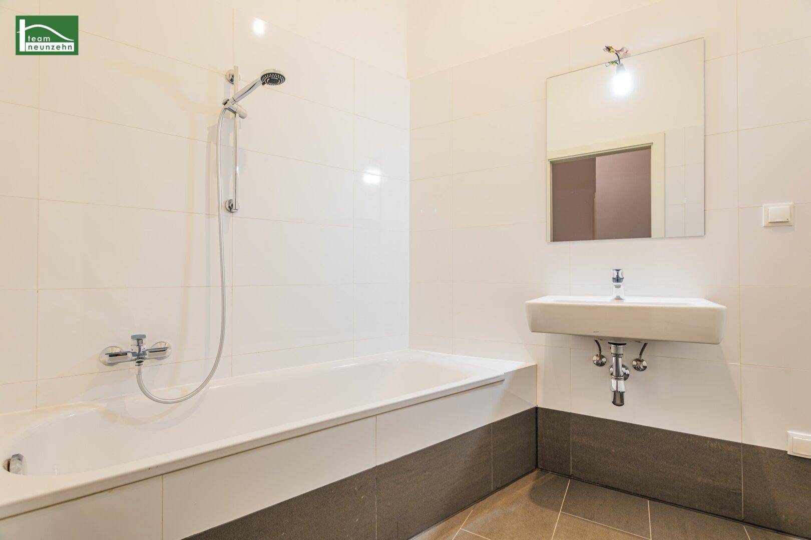 Modernes Badezimmer mit Badewanne, Duscharmatur und weiß-grauen Fliesen.