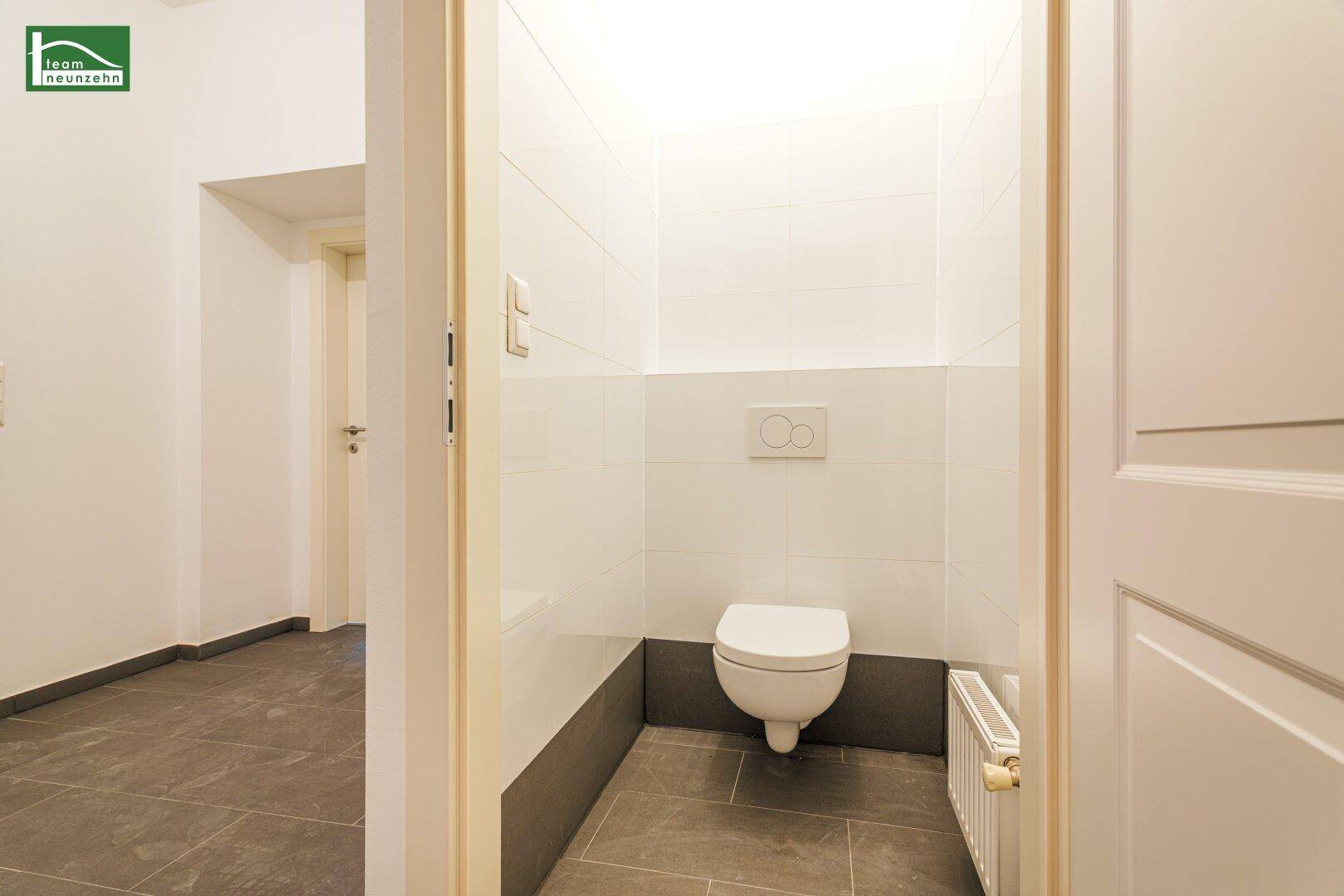 Separate Gästetoilette mit Wand-WC und Fliesen an den Wänden und auf dem Boden.