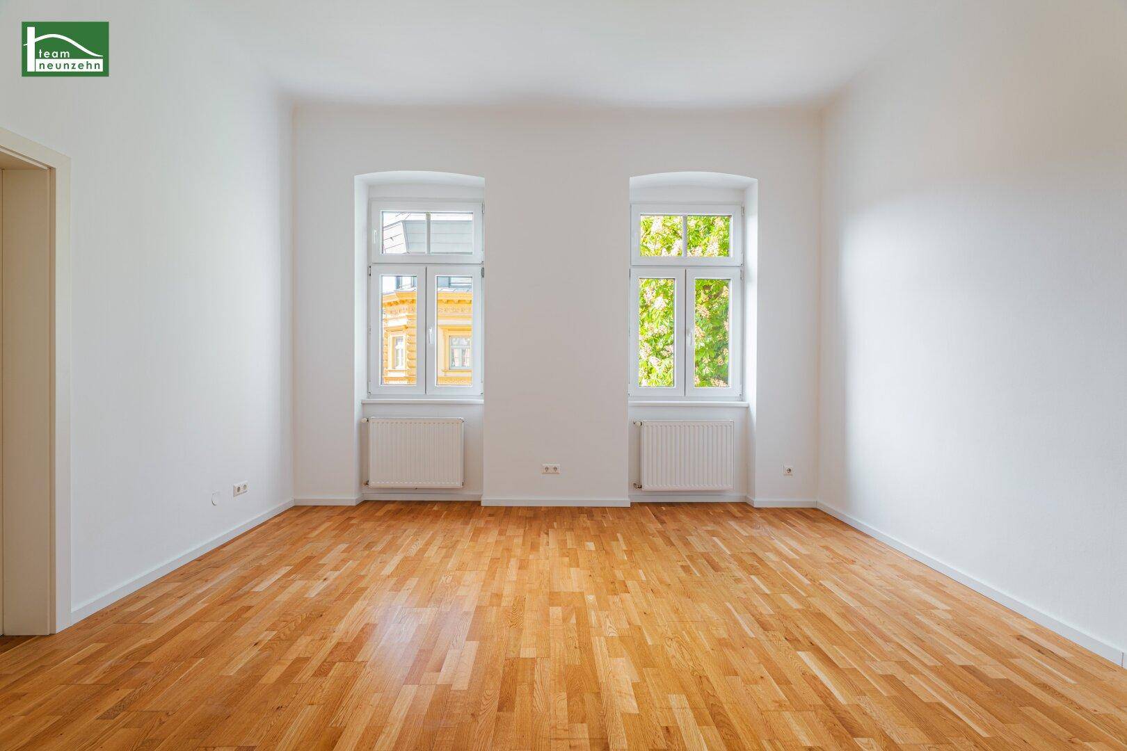 Lichtdurchflutetes Zimmer mit zwei großen Fenstern und klassischem Parkettboden.