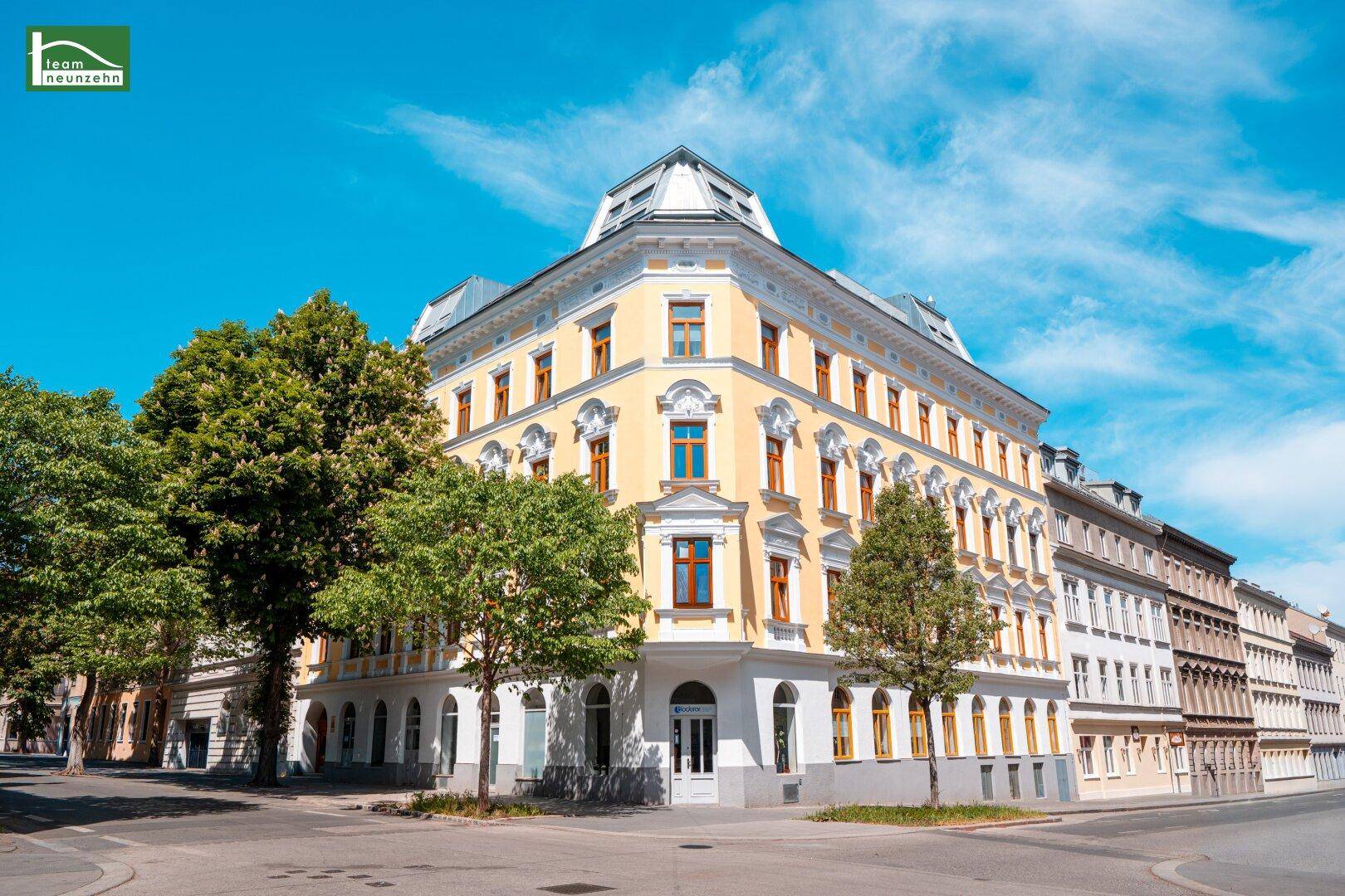 Historisches Eckgebäude mit gelber Fassade und Mansarddach in städtischer Umgebung.