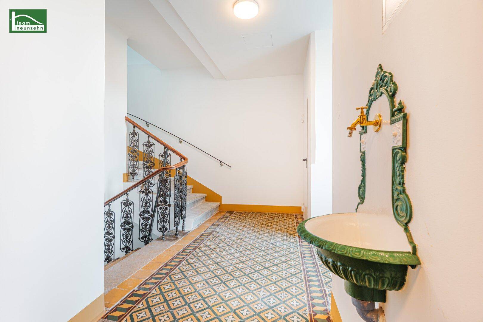Historischer Flur mit kunstvollen Fliesen, schmiedeeisernem Geländer und dekorativem Wandbrunnen.