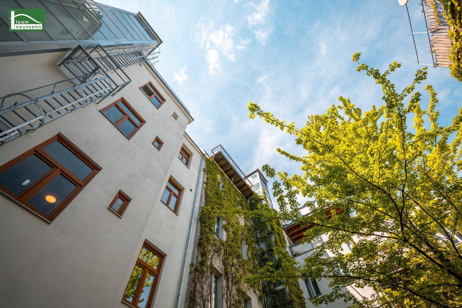 Fassade eines Gebäudes mit Efeubewuchs und großen Fenstern unter blauem Himmel.