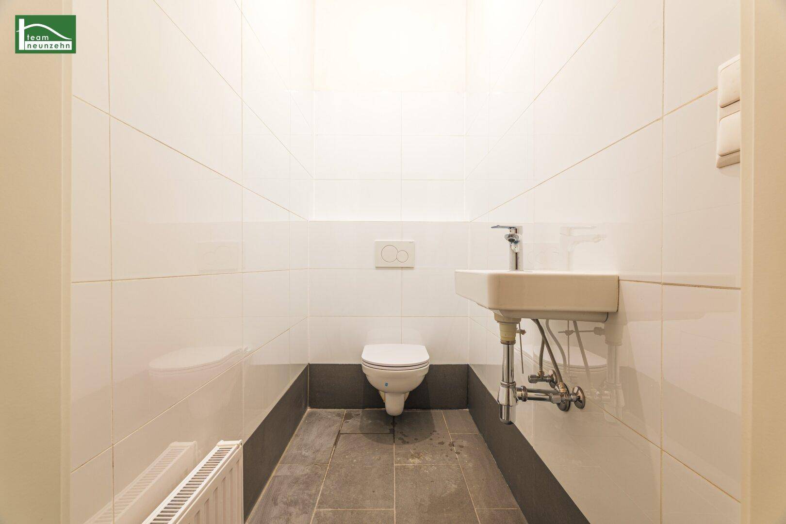 Modernes Gäste-WC mit weißen Fliesen, wandhängendem WC und kleinem Waschbecken.
