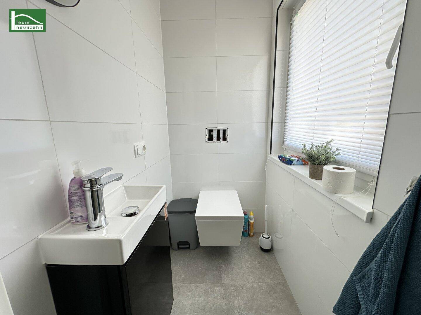 Modernes Gäste-WC mit weißen Fliesen, wandhängendem WC und kleinem Waschbecken.