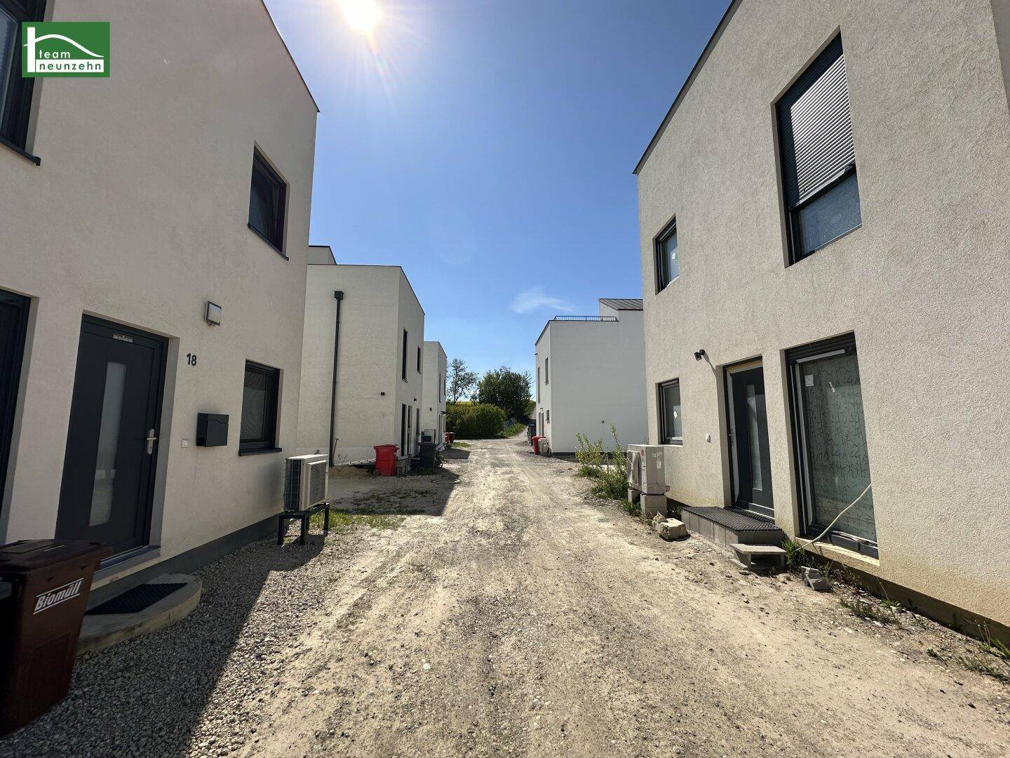 Reihe moderner Häuser entlang eines Schotterwegs unter strahlendem Sonnenschein.