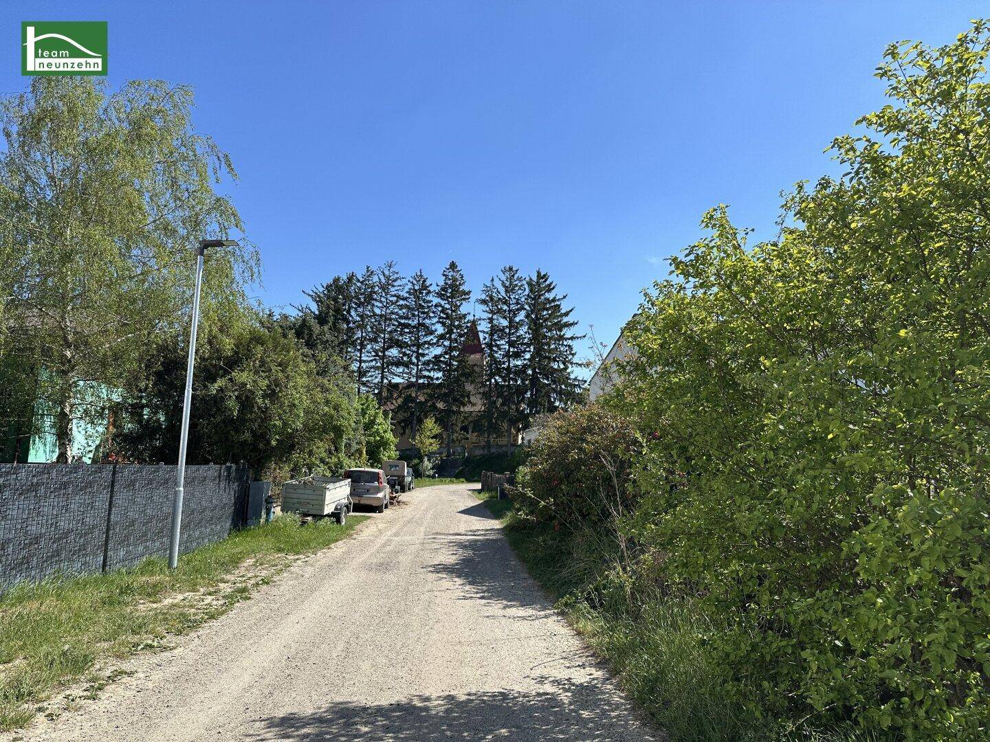 Schotterweg führt durch eine grüne Landschaft mit Bäumen und einem entfernten Gebäude.