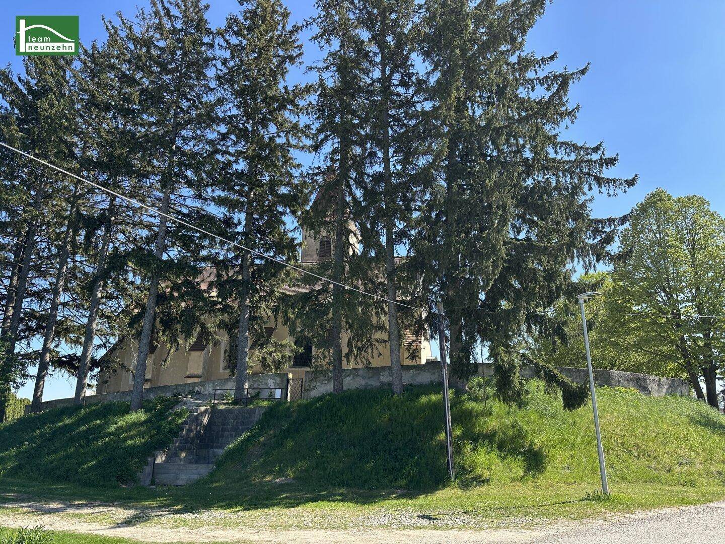 Historisches Gebäude, umgeben von hohen Bäumen und grüner Vegetation.