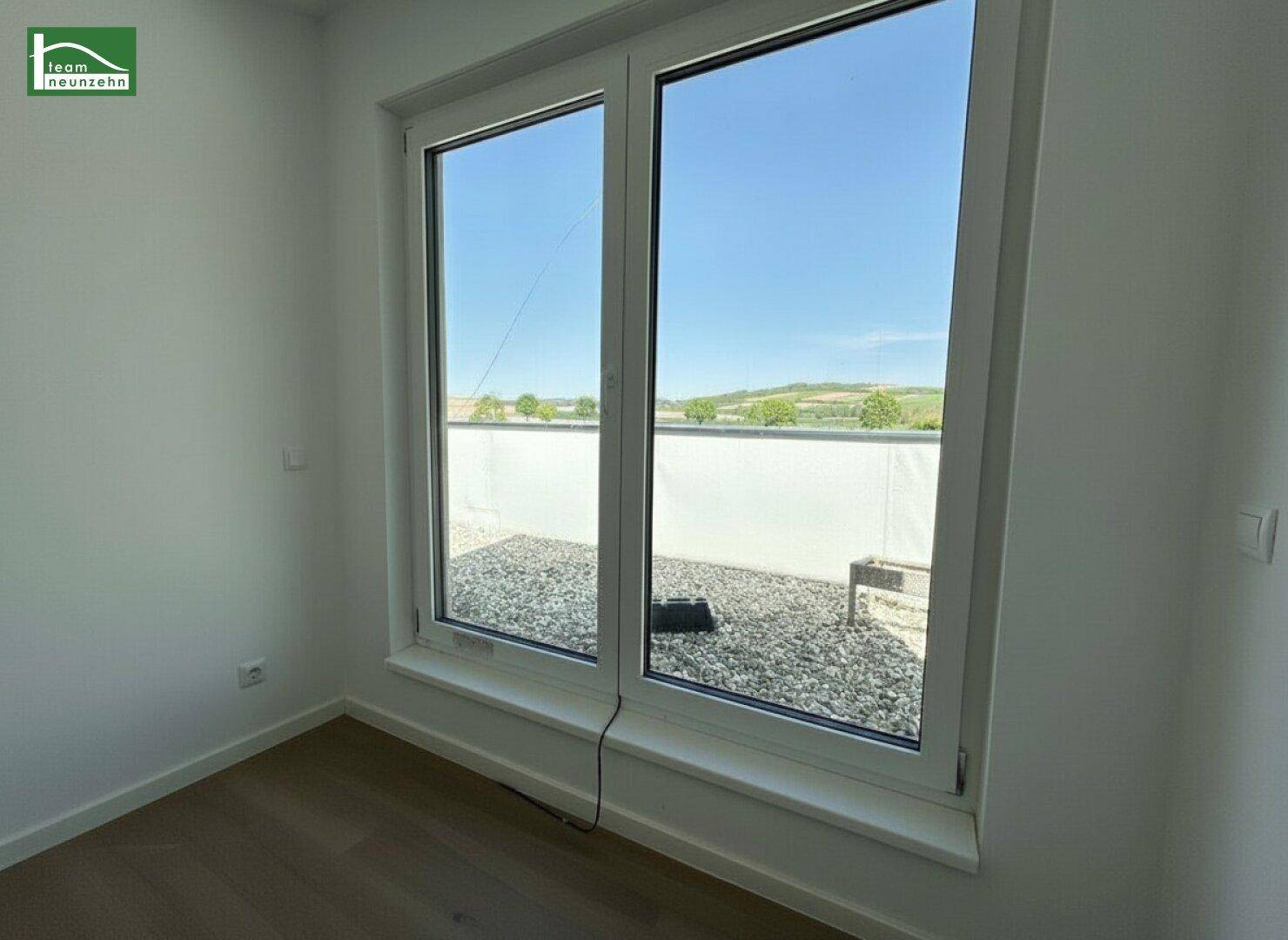 Helles Zimmer mit Holzboden und Zugang zu einer Kies-Dachterrasse.