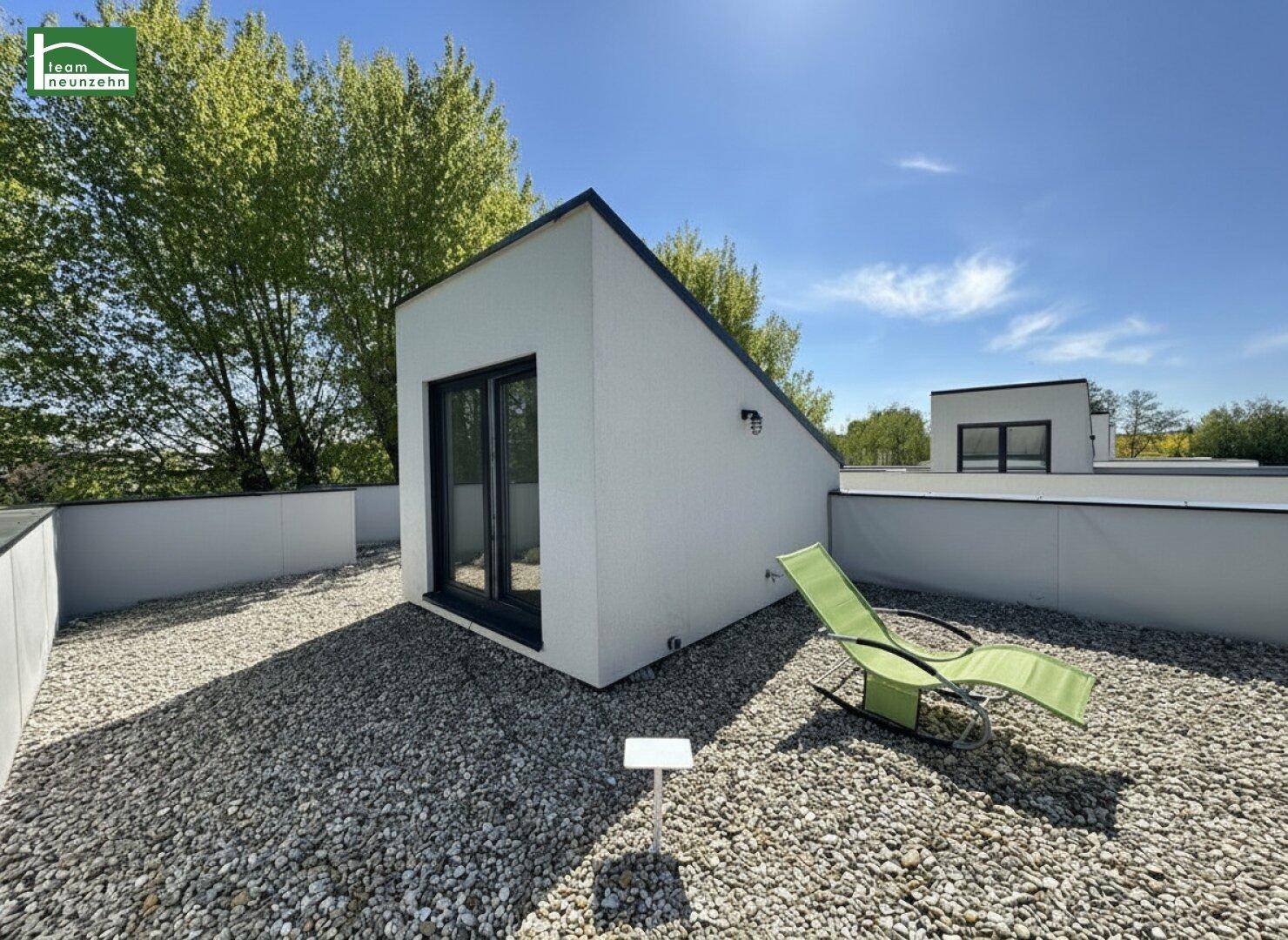 Geräumige Dachterrasse mit Kiesbelag und Liegestuhl unter blauem Himmel.