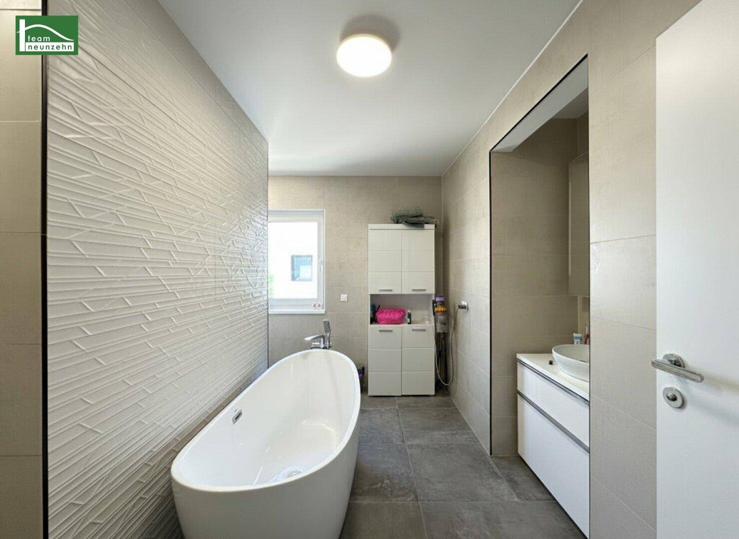 Modernes Badezimmer mit freistehender Badewanne, strukturierten Wandfliesen und Waschtisch.
