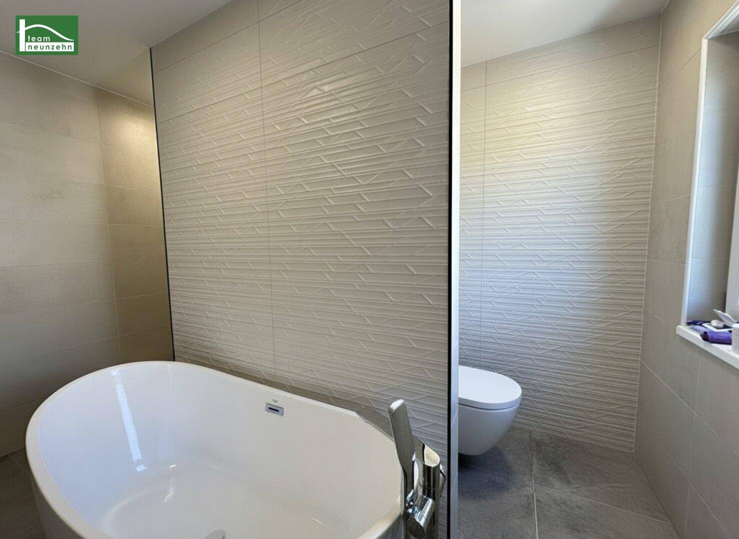 Modernes Badezimmer mit freistehender Badewanne, strukturierten Fliesen und wandhängendem WC.
