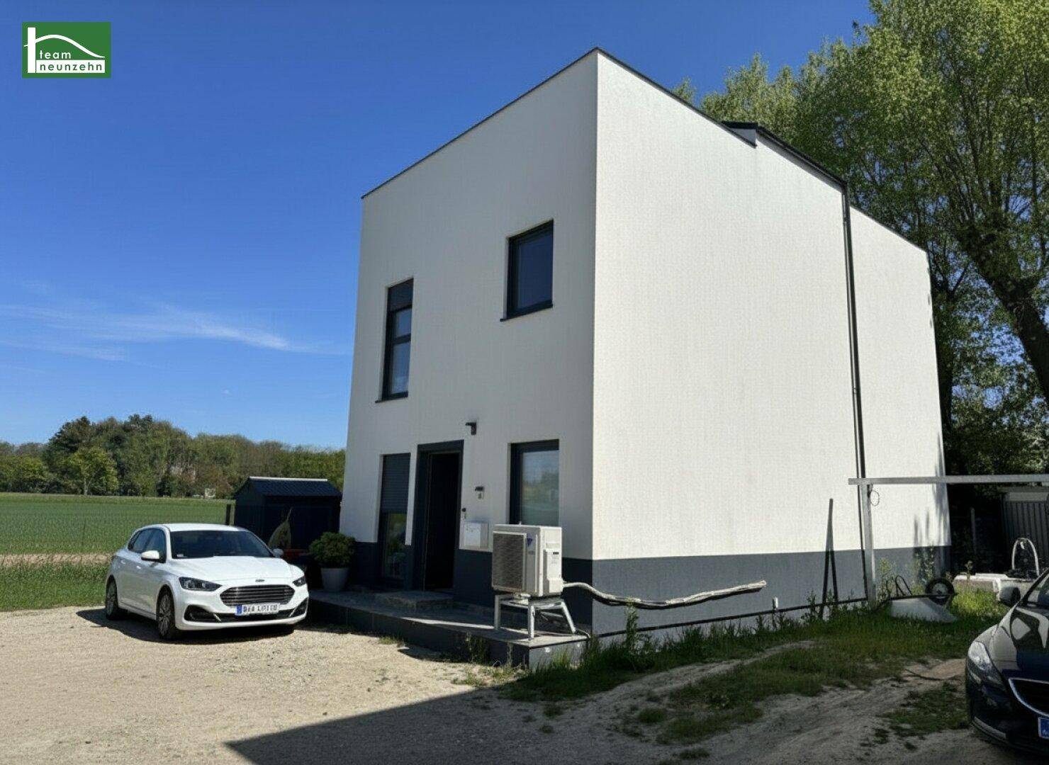 Seitenansicht eines modernen Hauses mit weißer Fassade und geparktem Auto.