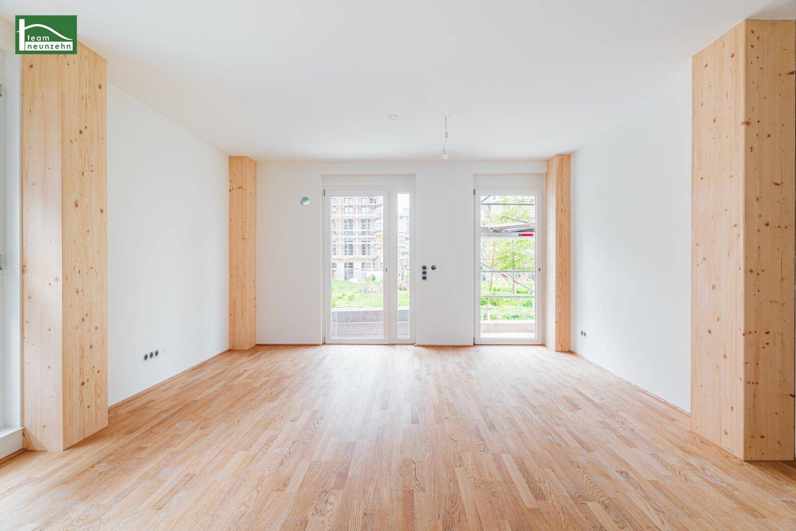 Heller, leerer Raum mit Holzboden und zwei Fenstertüren, die ins Freie führen.