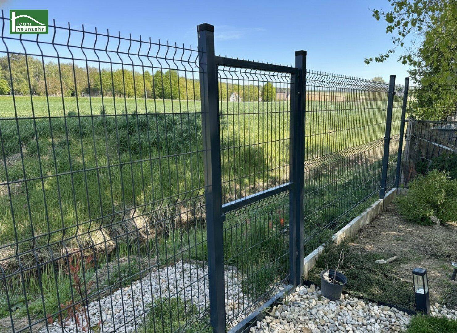 Robuster Metallzaun begrenzt den Gartenbereich mit Blick auf grüne Wiesen.