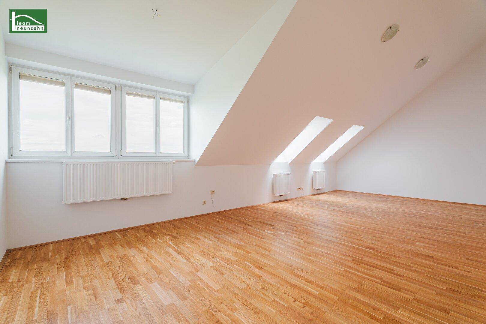 Lichtdurchfluteter Dachgeschossraum mit breiter Fensterfront, Holzboden und schrägen Decken.