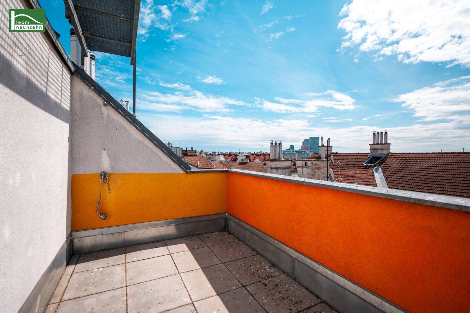 Sonnige Dachterrasse mit farbiger Brüstung und weitem Blick über die Dächer der Stadt.