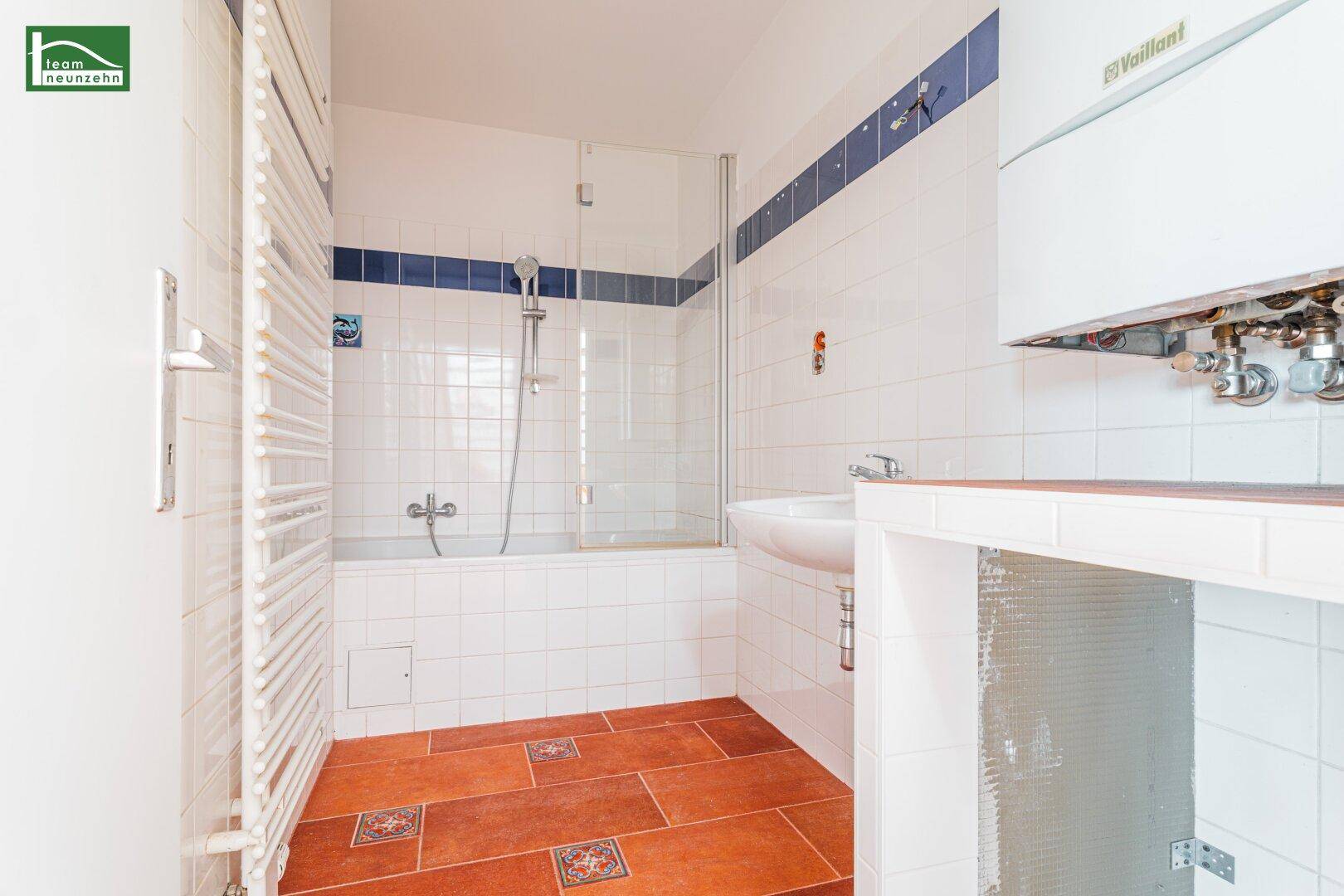 Gefliestes Badezimmer mit Badewanne, Duschwand, Waschbecken und praktischem Handtuchheizkörper.