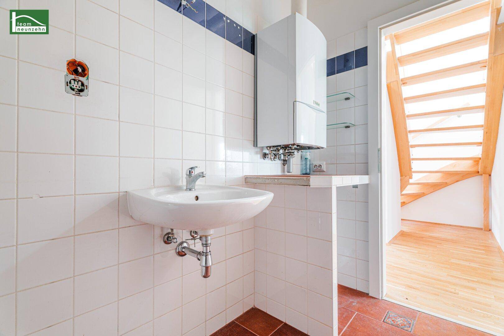 Badezimmer mit Waschbecken, Gastherme und weißen Wandfliesen, ergänzt durch einen Terrakotta-Boden.