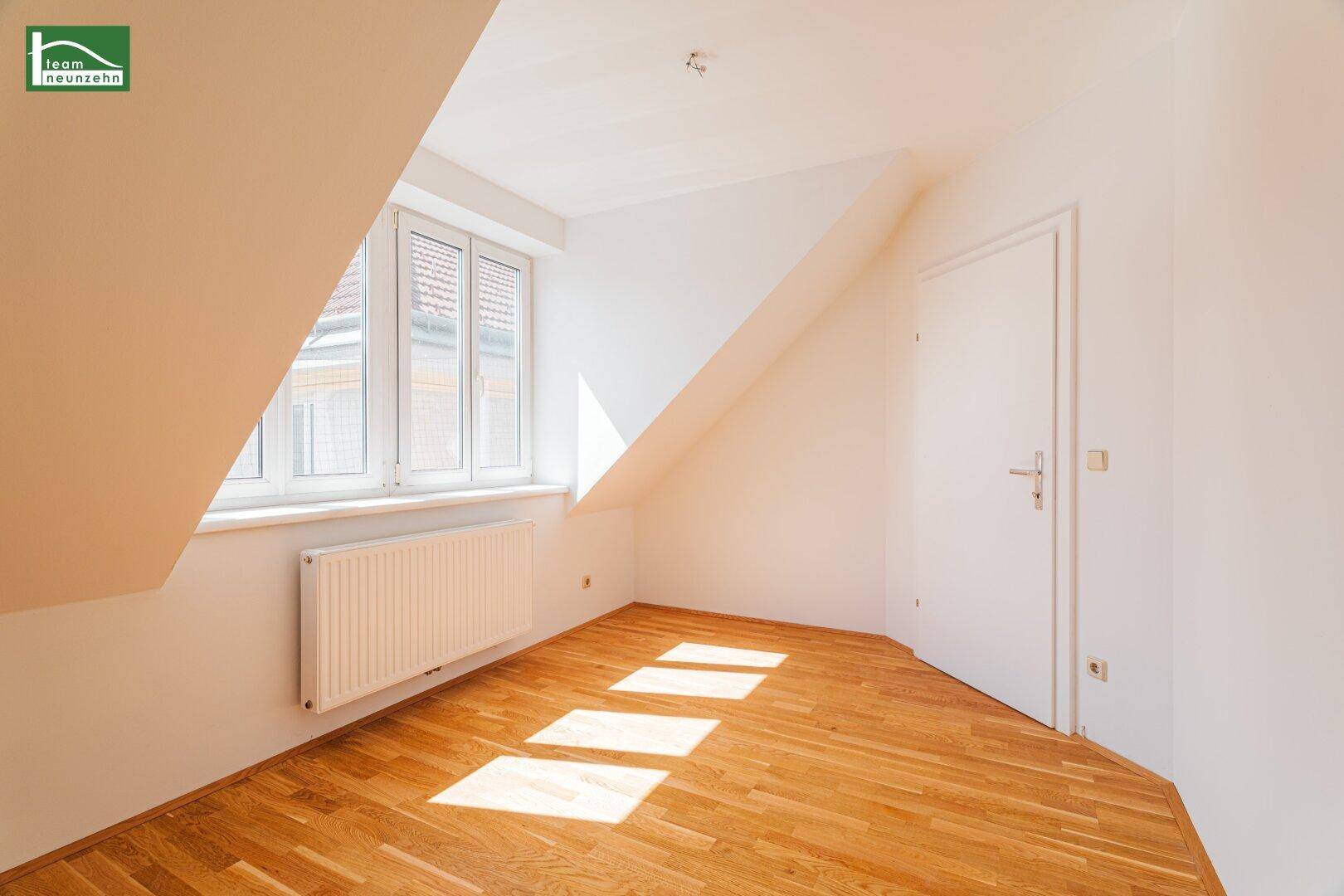 Helles Dachgeschosszimmer mit Holzboden und schräger Wand, durchflutet von Sonnenlicht, mit Zugangstür.