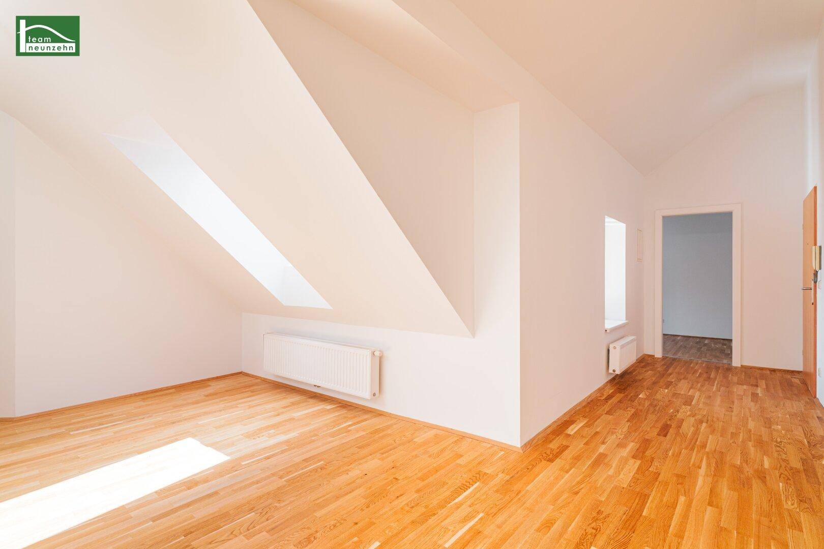 Offener Dachgeschossbereich mit Holzboden und schrägen Wänden, beleuchtet durch Dachfenster und Tageslicht.